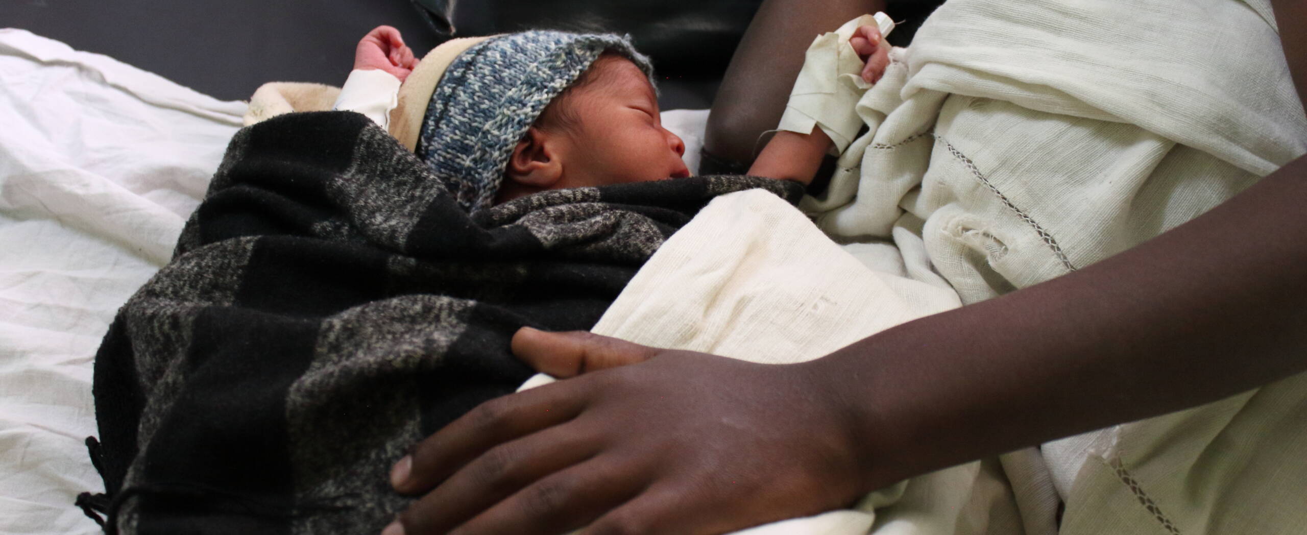 Schützende Hand einer Mutter liegt auf ihrem Neugeborenen in einem unserer Partnerspitäler