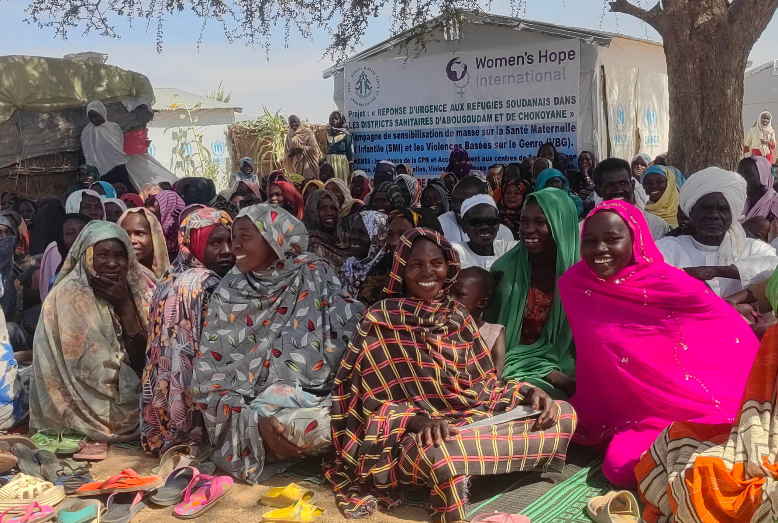 Frauen sitzen vor Zelten eines Flüchtlingslagers am Boden.